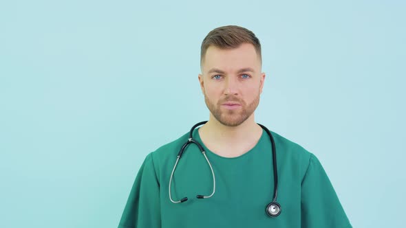 Successful Doctor Surgeon in Green Uniform Blue Gloves and Stethoscope Looks at Camera on Blue