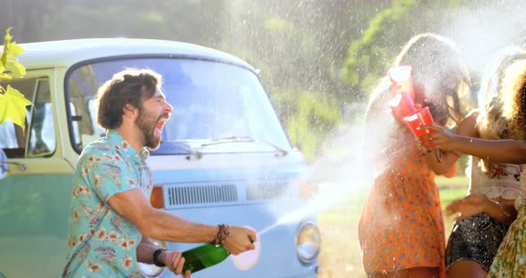 Hipster man cracking open a bottle of champagne on his friends