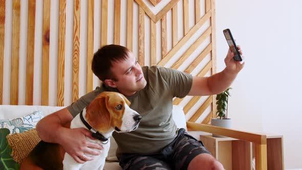 A Joyful Young Man Sitting at Table and Hugging Her Dog Beagle While Making Video Call