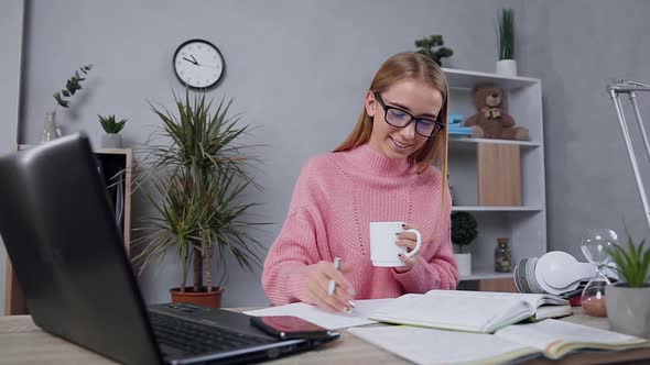 Blond Girl in Pink Sweater writing Out Necessary Notes from Book Into Notebook 