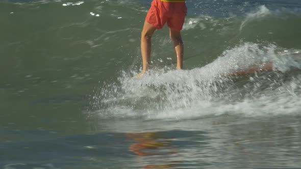 A male surfer riding a wave and doing a hang-5 trick on a longboard surfboard.