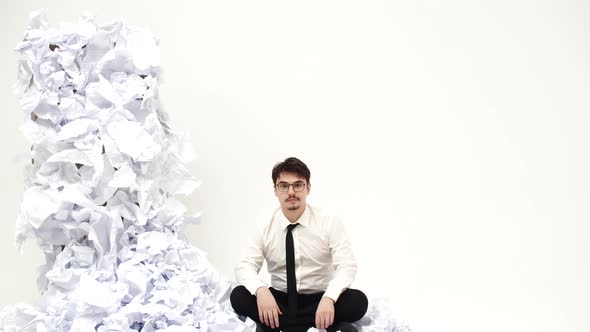 Man is sitting next to pile of crumpled documents and spreads hands to sides, front view