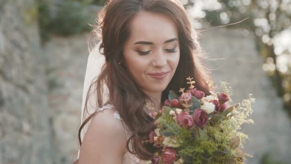 Happy Bride with Bouquet in Hands Smiles and Poses at Ancient Castle