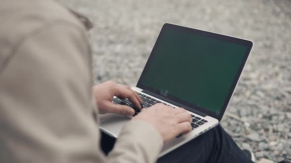 Close Up Shot of a Man's Hands Who Work on a Laptop Outdoors Among a Rocky Beach