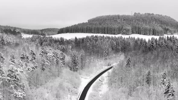 Winter and snowy white trees. Drone shot flyings backwards over a valley with a curvy street in the