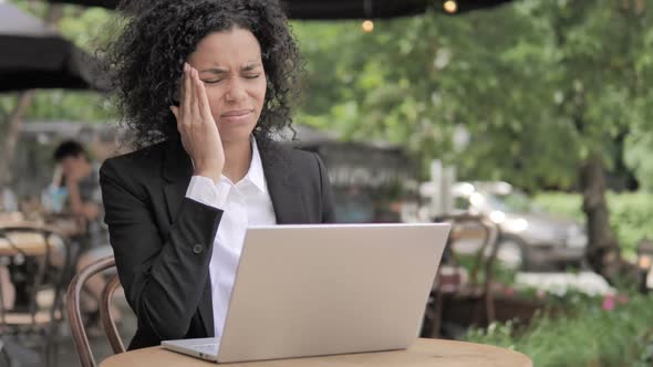 African Woman with Headache Using Laptop in Outdoor Cafe