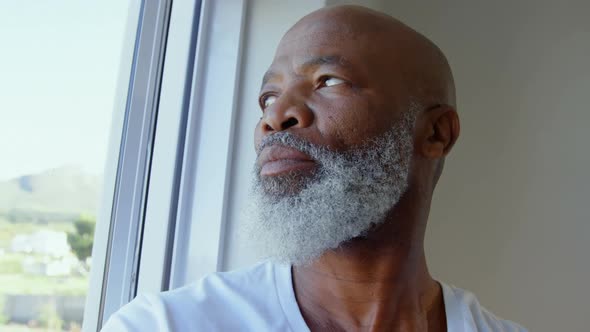 Side view of mature black man looking through window in a comfortable home 4k