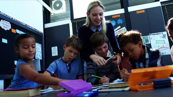 Teacher helping schoolkids with their homework in classroom