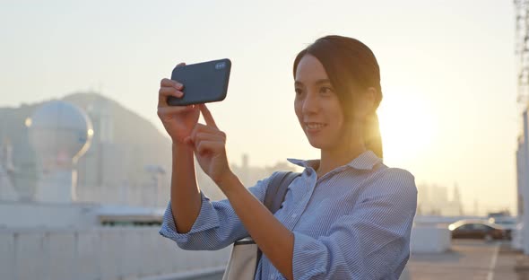 Woman take photo on cellphone in city at sunset