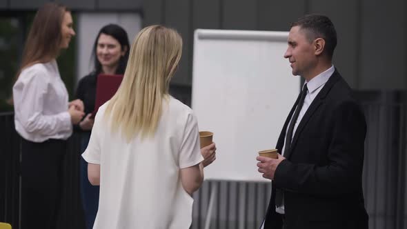 Positive Confident Man and Woman Talking and Walking to Colleagues Standing at Background