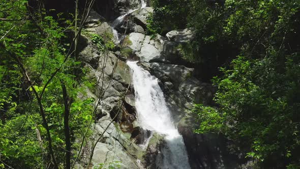 Drone Ascending Close through Green Shrubs with Saltos Jima Waterfall Flowing off a Small Rocky Clif