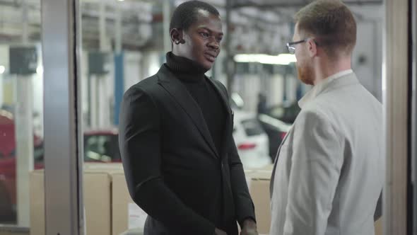 Young Cheerful African Americam Car Dealer Giving Keys To Successful Caucasian Redhead Man in