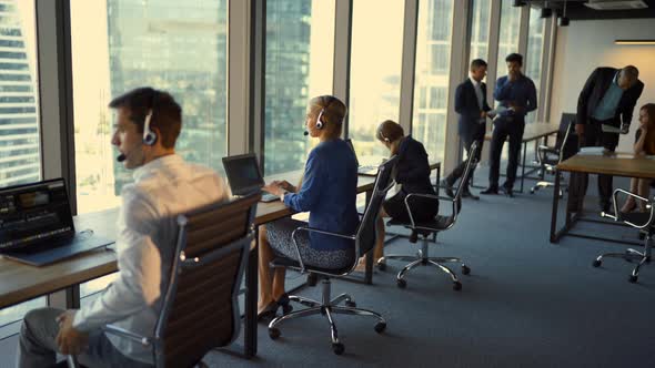 Back View of Handsome Young Businessman and Beautiful Business Women in Headsets Using Laptops While