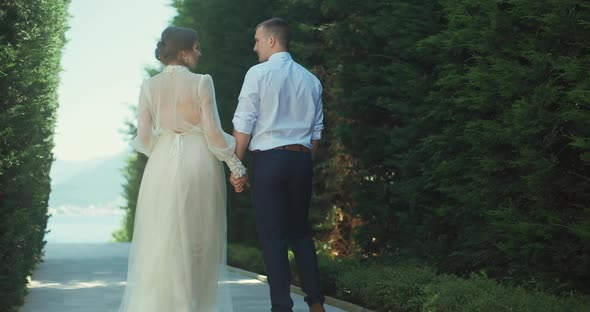 Newlyweds walk and hold hands in the park on a summer day.