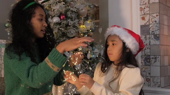 Daughter Wraps Mother with Light Garland By Christmas Tree