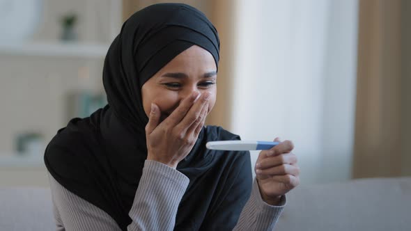 Portrait Joyful Surprised Girl in Hijab Holding Pregnancy Test Sit in Living Room Excited with