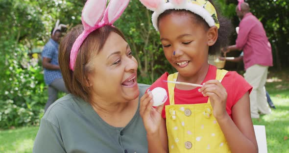 Animation of happy african american grandmother and granddaughter painting easter eggs in garden