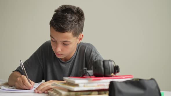 Caucasian Boy Sitting at Table with Workbook and Looking at Tablet Screen While Attentively