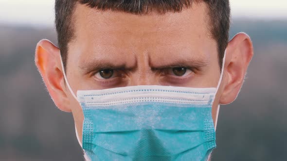 Young Man in a Medical Protective Face Mask Looking at the Camera on the Street Background