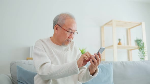 Asian senior elderly male using mobile phone in living room at home.