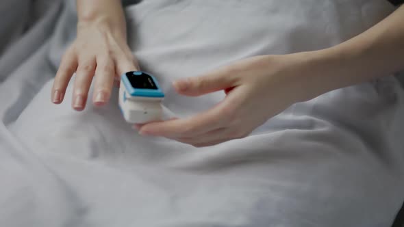 Woman lying at a bed using a pulse oximeter at the index finger.