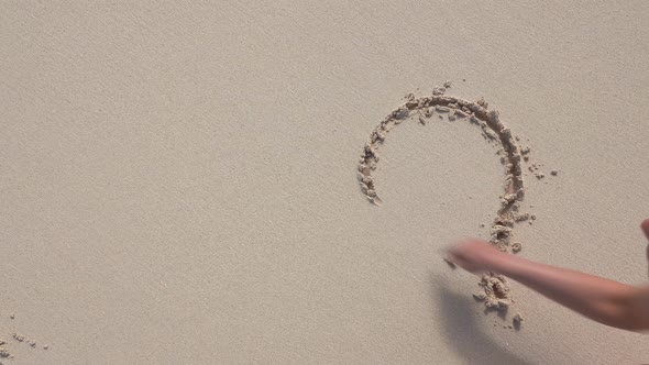 Woman's hand drawing a heart on the sand