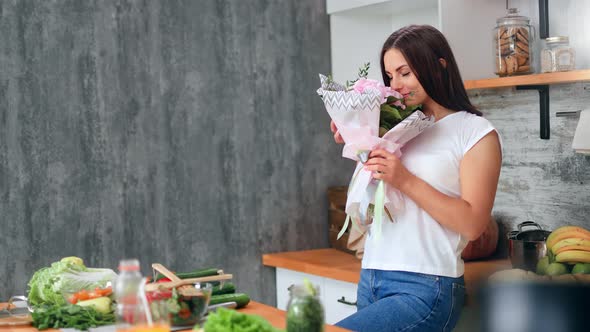 Adorable Casual Young Girl Sniffing Pink Gentle Flower Bouquet in Kitchen at Home