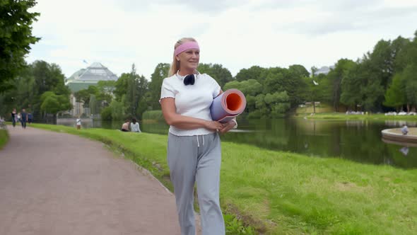 Aged Woman Strolling with Mat Ready for Yoga at Park