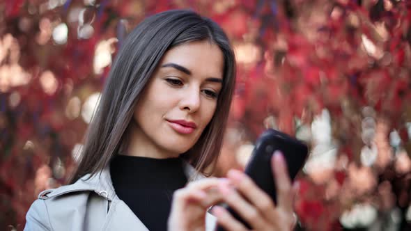 Happy Female Face Chatting Use Smartphone at Red Fall Foliage Bokeh