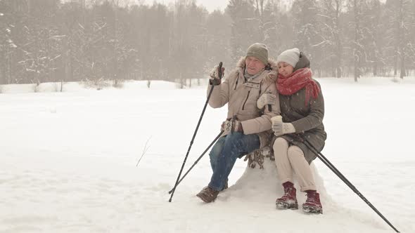 Senior Couple Sitting on Stump in Winter alt