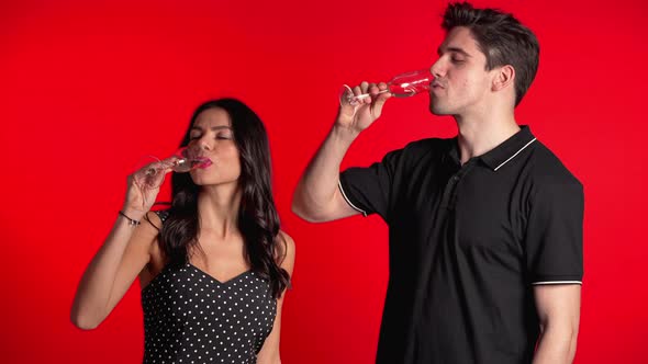 Portrait of Young Couple Drinking Champagne on Red Studio Background.