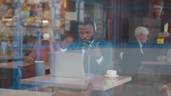 View Through Window of AfricanAmerican Businessman Having Video Call on Laptop in Cafe