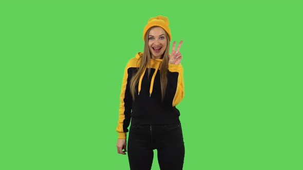 Modern Girl in Yellow Hat Is Showing Two Fingers Victory Gesture. Green Screen