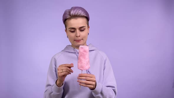 Cheerful Young Adult Woman Eating Candy Floss with Pleasure Indoors