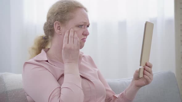 Close-up of Woman Examining Wrinkles on Face. Side View of Senior Caucasian Lady Dissatisfied with