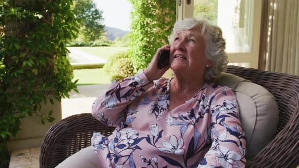 Caucasian senior woman talking on smartphone while sitting on the chair outdoors