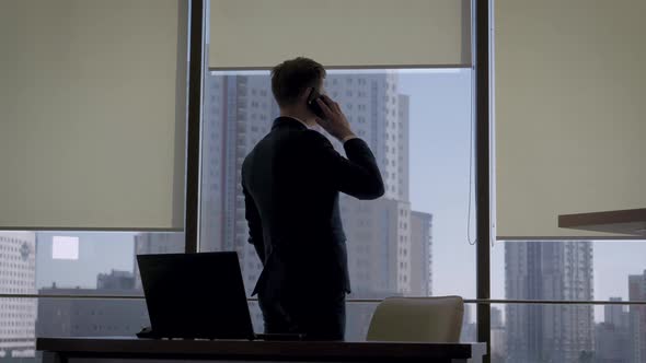 Director In A Business Suit Talking On Phone At Office Window Near To Workplace