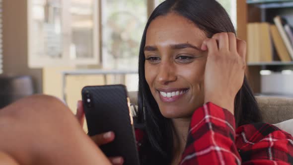 Mixed race woman using smartphone, having a video conversation sitting on couch