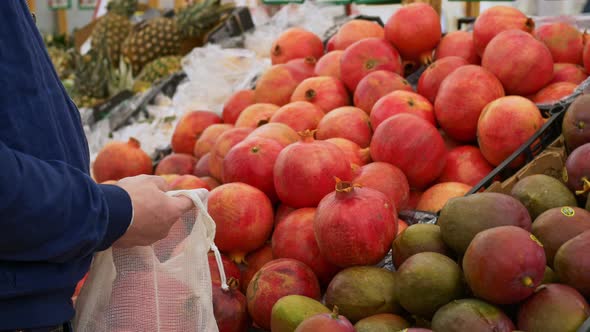 A Man in the Market Buys Fresh Fruits Chooses Ripe Pomegranates for the Whole Family