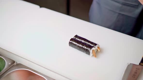 Male Chef Hands Cutting Prepared Maki Sushi Roll on Board in Restaurant Kitchen