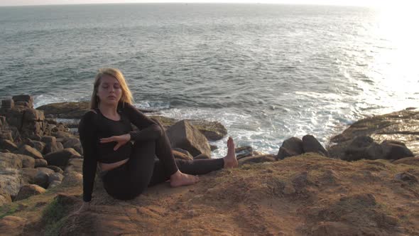 Pretty Girl in Black Tracksuit Sits on Grey Rocky Cliff