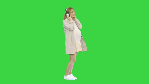 Pregnant Woman Standing and Listening Dancing Music in Headphones on a Green Screen, Chroma Key.