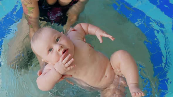 Happy Mother in Red Swimming Suit with Baby Son Surfing Water with Fun in Swimming Pool