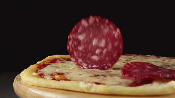 Salami Slices Fall On A Rotating Pizza On A Black Background