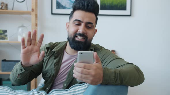 Cheerful Middle Eastern Guy Making Online Video Call Waving Hand and Talking Using Smartphone at