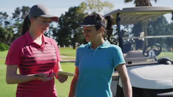 Two caucasian women playing golf talking writing in notebook