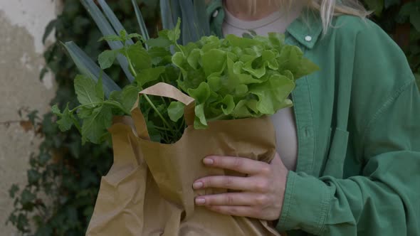 Smiling woman with vegetables in bag on ivy wall background