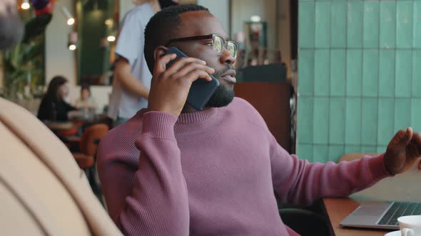 African Businessman Speaking on Phone in Cafe