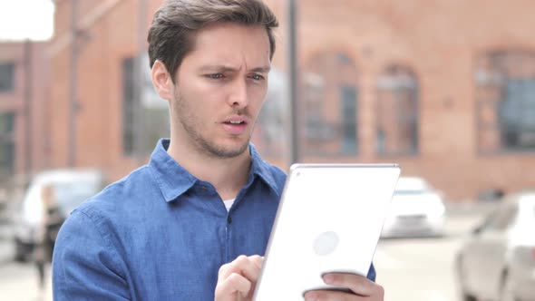 Outdoor Portrait of Upset Young Man Using Tablet