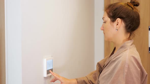 Happy Woman Presses Keys of Climate Control Panel in Hotel